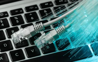 Cables de red y fibra óptica sobre un teclado de ordenador portátil, representando opciones de conexión ADSL para empresas.